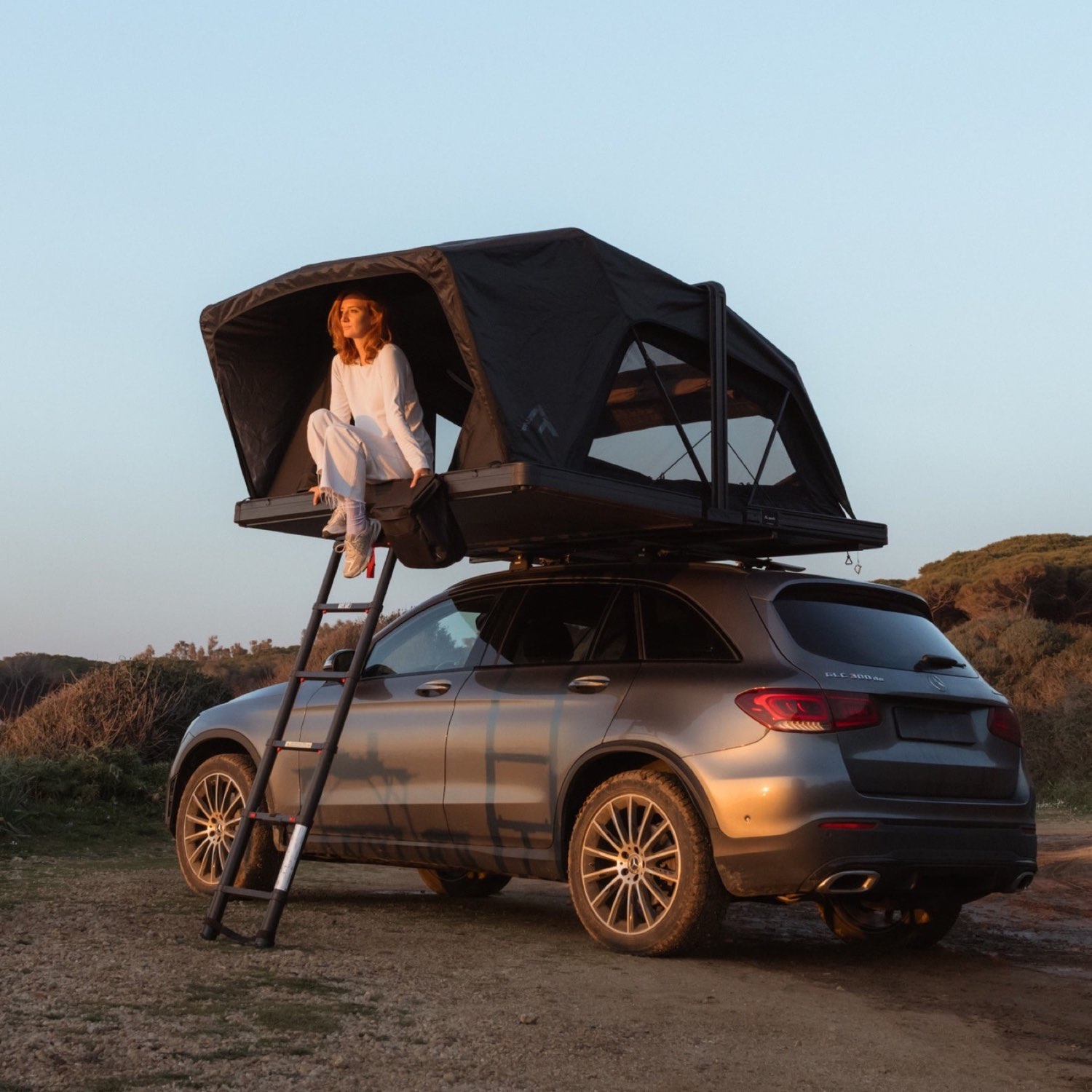 Dachzelt mit Leiter auf einem SUV im Abendlicht über dem Meer